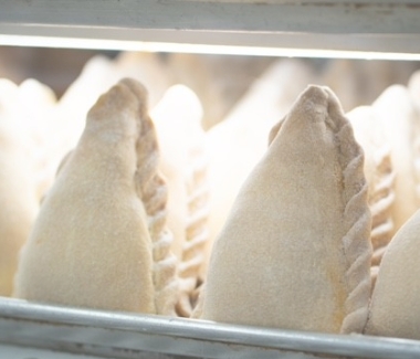 Hand-crimped artisanal empanadas on a floured baking table